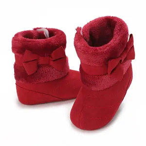 Close-up detail of cozy red baby winter boots featuring plush lining and large bow decoration.
