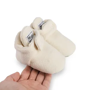 Close-up view of warm cream fleece baby booties featuring a Magic brand label on white