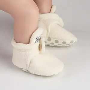 Detailed view of warm cream plush baby booties with anti-slip green dotted soles