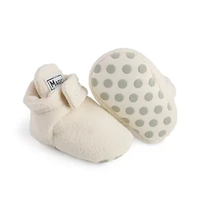 Soft cream white fleece-lined baby booties with green non-slip polka dot soles for infants.