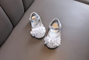 Close-up detail of silver rhinestone princess shoes for girls with elegant white fabric flowers