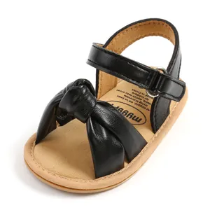 Close-up van zwarte leren baby sandaal met een stijlvolle strik en een handige klittenband.