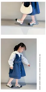 Little girl wearing black and white patent leather Mary Jane shoes in a denim dress.