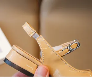 Macro view of the elastic slingback strap and chain detail on beige patent leather sandals.