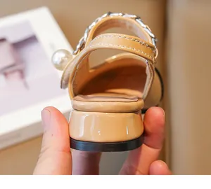 Close-up of beige patent leather girl's sandal with pearl and silver chain detail
