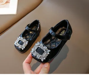 Detail shot of black patent leather girls shoe with shimmering crystal square buckle decoration.