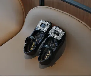 Detail of black patent leather girls' shoes with a large sparkling rhinestone buckle.