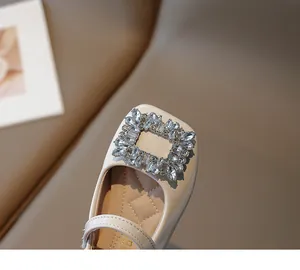 Close-up of sparkling rhinestone square buckle on cream patent leather girls' shoes