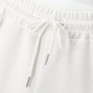 Close-up of white waffle knit pants waistband featuring drawstring and metal tips