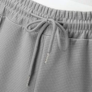 Close-up of grey waffle knit trousers featuring elastic waistband and drawstring detail