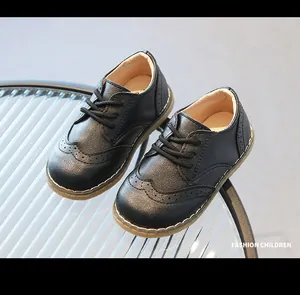 Detail of black textured leather children's brogue shoes on a glass table.