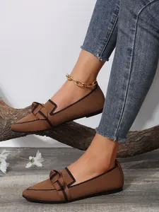 Close-up of brown pointed-toe knitted flat shoes with bow detail on a model's feet
