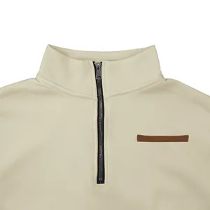 Detalle de una sudadera crema para hombre con media cremallera, cuello alto y tira decorativa.