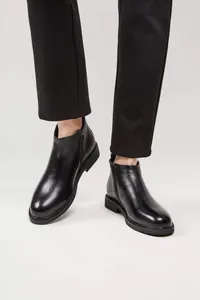 Nahaufnahme von stilvollen schwarzen Chelsea-Boots aus Leder mit schwarzer Hose