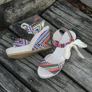 Detailed view of ethnic wedge sandals with geometric prints and ribbon ties on wood.