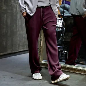 Detalle de pantalones plisados granate para hombre con rayas verticales y cordón ajustable