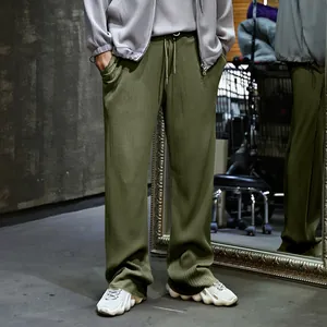Vista detallada de pantalones plisados de pernera ancha para hombre en verde oliva.