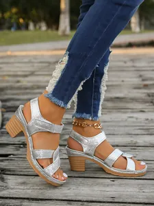 Detalle de sandalias plateadas de tacón alto con tiras cruzadas y cierre de velcro.