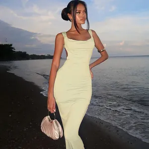 Elegant backless bodycon midi dress in pale lime green worn by a model on a sunset beach