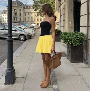 Detail view of a black tube top and yellow pleated skirt color-block slim fit mini dress