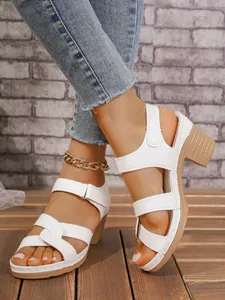 Detalle de sandalias blancas de tacón grueso con tiras cruzadas y velcro.
