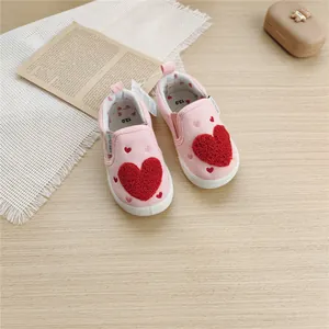 Top view of pink baby canvas walking shoes featuring plush red heart patches on wood