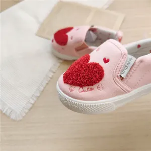 Detail view of pink baby canvas walking shoes with a red plush heart and logo tag