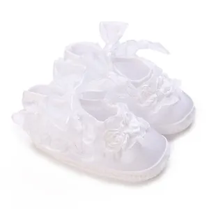 Detailed view of white soft-sole baby baptism shoes with delicate lace and bows.