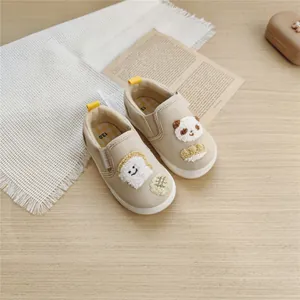 Close-up of beige toddler canvas shoes featuring cute bread and panda embroidery detail.