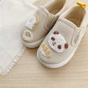 Close-up detail of beige canvas toddler shoes with cute panda and toast appliques.