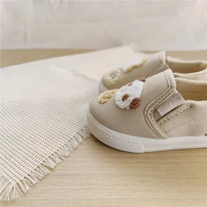 Detailed view of beige kids canvas slip-on shoes with soft soles and 3D puppy embroidery