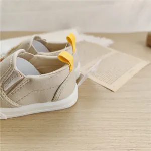 Close-up of beige children's soft-sole canvas shoes with vibrant yellow pull tabs