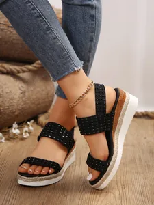 Primer plano de correas negras texturizadas en sandalias de cuña trenzadas para mujer.