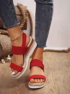 Primer plano de sandalias de cuña rojas con correas trenzadas de pedrería.