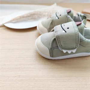 Détail du motif de dinosaure de dessin animé sur des chaussures de bébé vert sauge