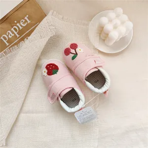 Overhead view of pink baby walking shoes with strawberry and cherry embroidery