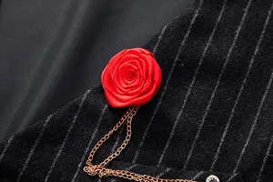 Close-up of a red satin rose brooch with gold chains on a striped vintage men's vest