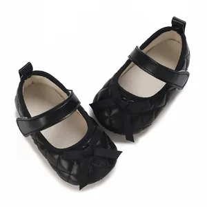 Detalle de zapatos negros acolchados para bebé con un lazo decorativo y cierre de velcro