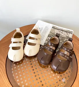 Zapatos de bebé tipo Tabi de cuero en beige y marrón oscuro sobre una mesa.