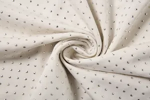 Vue macro du tissu de robe crème orné d'un motif dense de strass argentés brillants
