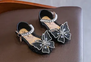Close-up of girls' black princess shoes featuring a rhinestone butterfly bow and pearls.