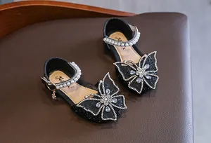 Detailed view of black glittery girls' sandals with large rhinestone butterfly embellishment