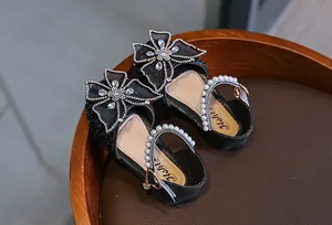 Close-up of girl's black princess sandals with rhinestone bow and pearl strap