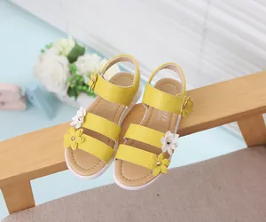 Elegantes sandalias de verano amarillas para niña con flores sobre silla madera