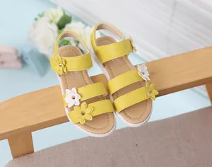 Sandalias amarillas de princesa para niñas con lindas flores en 3D sobre silla madera