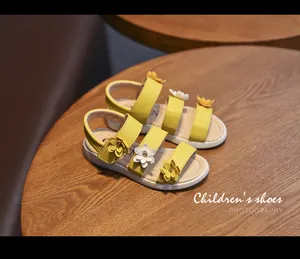 Close-up detail of yellow girl's sandals with decorative 3D floral accents on table.
