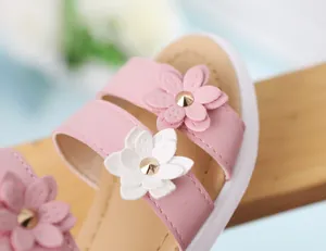 Primer plano de sandalias rosas para niñas con flores 3D y tachuelas doradas