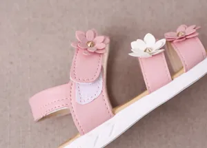 Primer plano de una sandalia rosa para niña con flores decorativas de cuero en 3D.