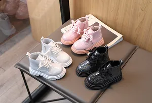 Three pairs of glittery kids Martin boots in pink, white, and black displayed on a bench