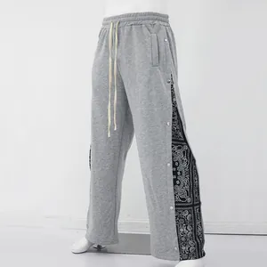 Détail d'un pantalon gris large avec boutons-pression et empiècements imprimé cachemire.